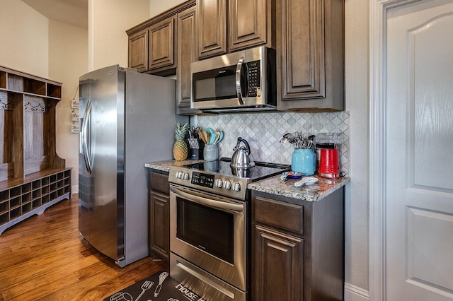 kitchen with tasteful backsplash, light stone counters, stainless steel appliances, and dark hardwood / wood-style floors