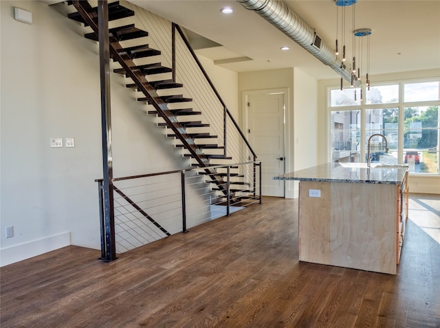 kitchen featuring pendant lighting, a center island with sink, light stone countertops, and dark wood-type flooring