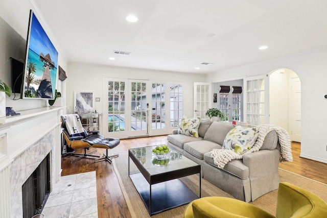 living room with a tiled fireplace, light wood-type flooring, and french doors