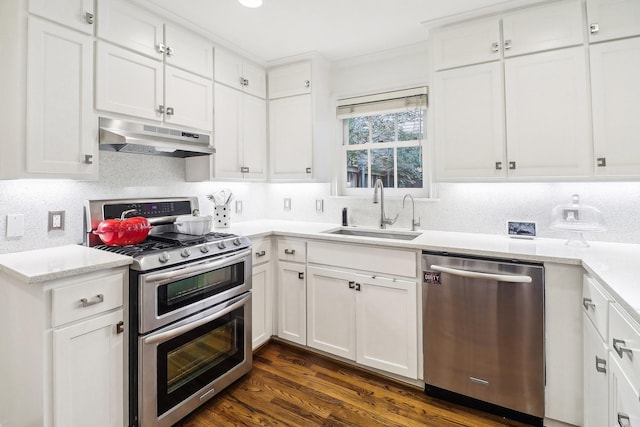 kitchen featuring appliances with stainless steel finishes, sink, white cabinets, dark hardwood / wood-style flooring, and decorative backsplash