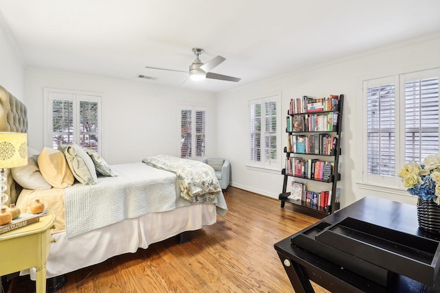 bedroom featuring hardwood / wood-style flooring, crown molding, ceiling fan, and multiple windows