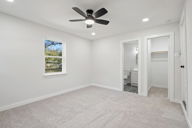 unfurnished bedroom with ensuite bath, ceiling fan, a spacious closet, light colored carpet, and a closet