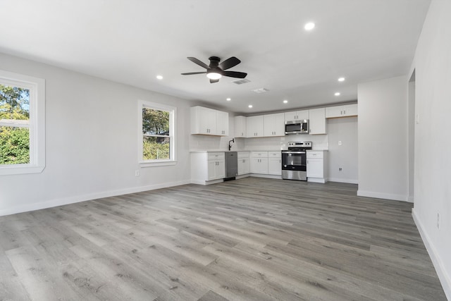 unfurnished living room featuring light hardwood / wood-style flooring, ceiling fan, a healthy amount of sunlight, and sink