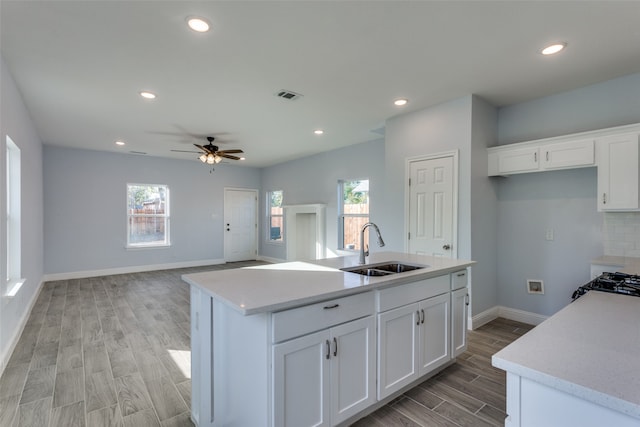 kitchen with ceiling fan, sink, white cabinets, and a center island with sink