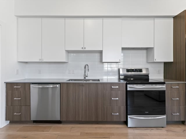 kitchen featuring light wood-type flooring, backsplash, stainless steel appliances, sink, and white cabinets