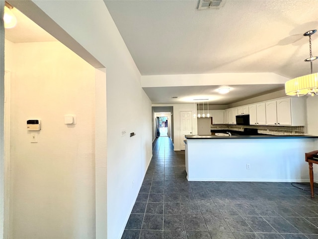 kitchen with hanging light fixtures, backsplash, kitchen peninsula, white cabinets, and dark tile patterned flooring