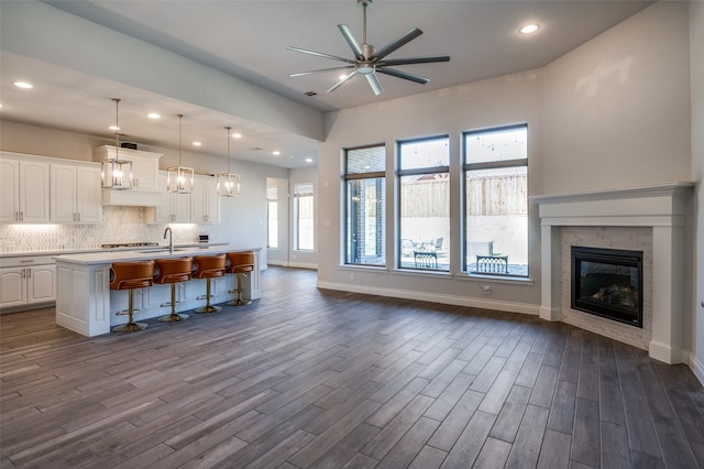 kitchen with a kitchen breakfast bar, dark hardwood / wood-style flooring, pendant lighting, a center island with sink, and white cabinets