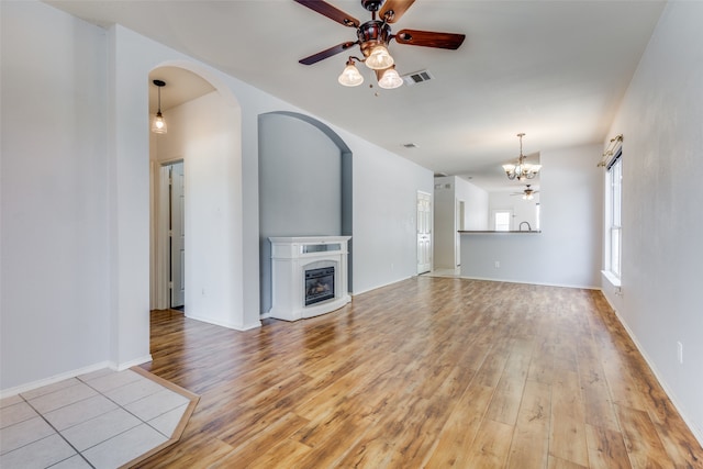 unfurnished living room featuring ceiling fan with notable chandelier and light wood-type flooring