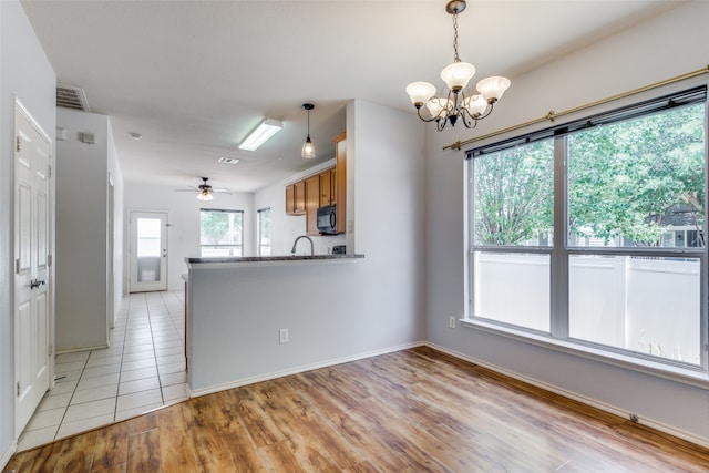 kitchen with kitchen peninsula, light stone counters, ceiling fan with notable chandelier, sink, and light hardwood / wood-style floors