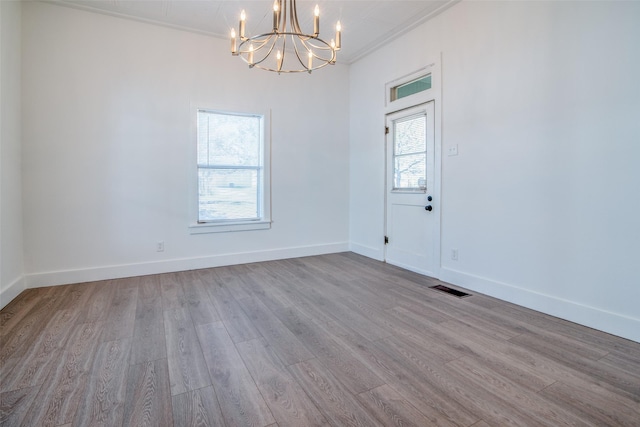 spare room with an inviting chandelier, crown molding, and light hardwood / wood-style flooring