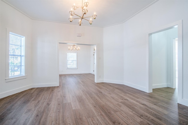 empty room featuring hardwood / wood-style flooring, ornamental molding, and a notable chandelier