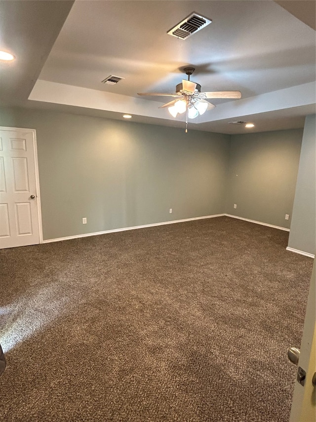 empty room with a tray ceiling, ceiling fan, and carpet floors