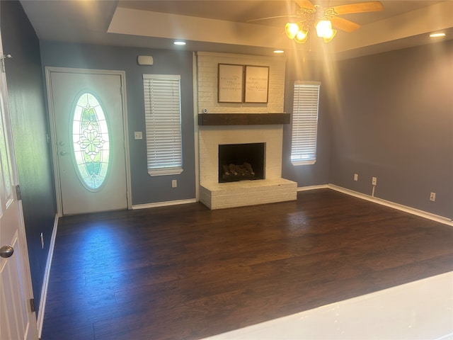 unfurnished living room featuring a brick fireplace, dark wood-type flooring, and ceiling fan