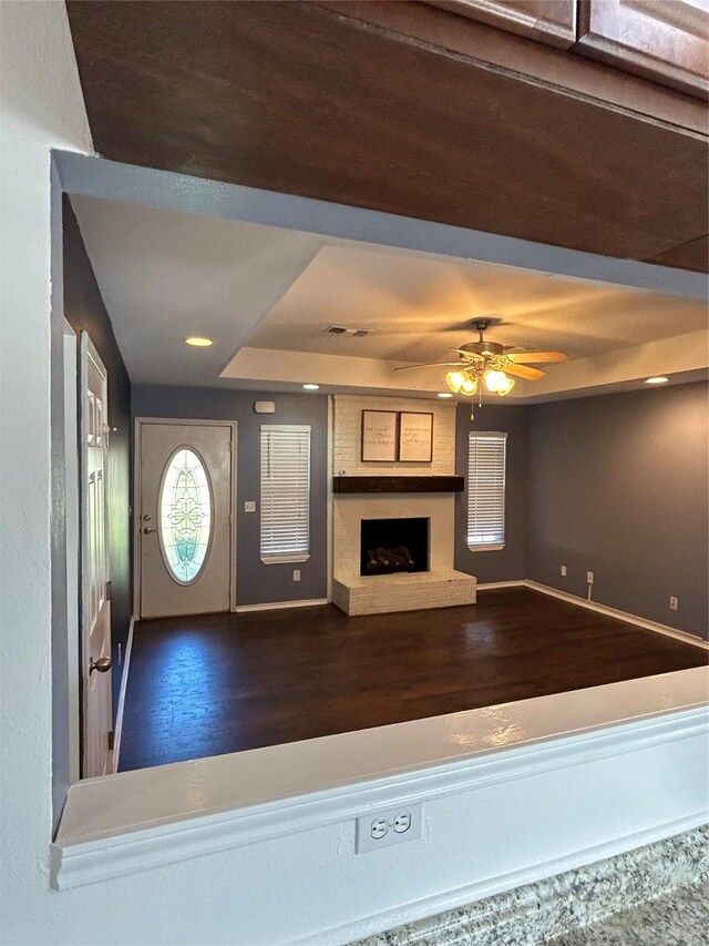 unfurnished living room featuring a raised ceiling, ceiling fan, and dark wood-type flooring