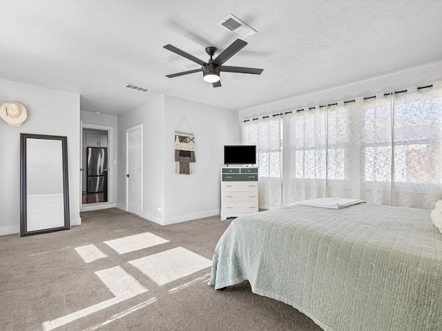 bedroom featuring ceiling fan, light colored carpet, stainless steel refrigerator, and a textured ceiling