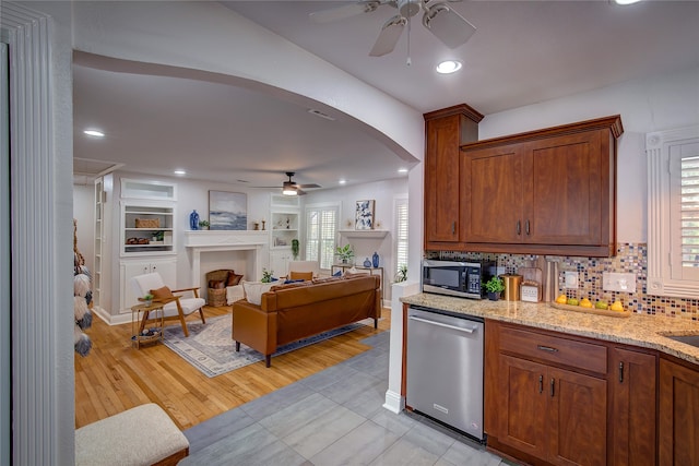 kitchen featuring ceiling fan, light stone counters, light hardwood / wood-style floors, decorative backsplash, and appliances with stainless steel finishes