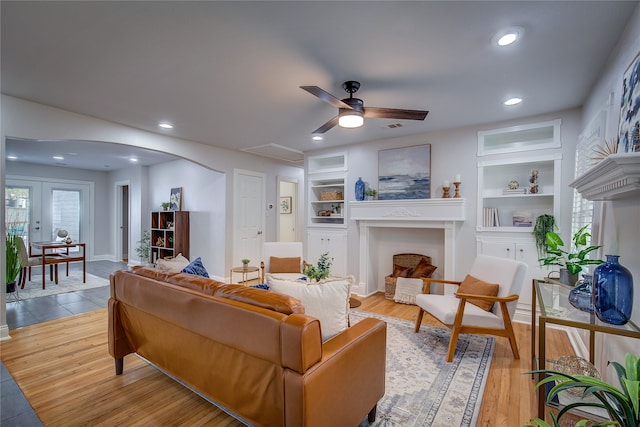 living room with built in features, french doors, light hardwood / wood-style flooring, and ceiling fan