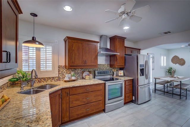 kitchen with wall chimney range hood, sink, decorative backsplash, appliances with stainless steel finishes, and decorative light fixtures