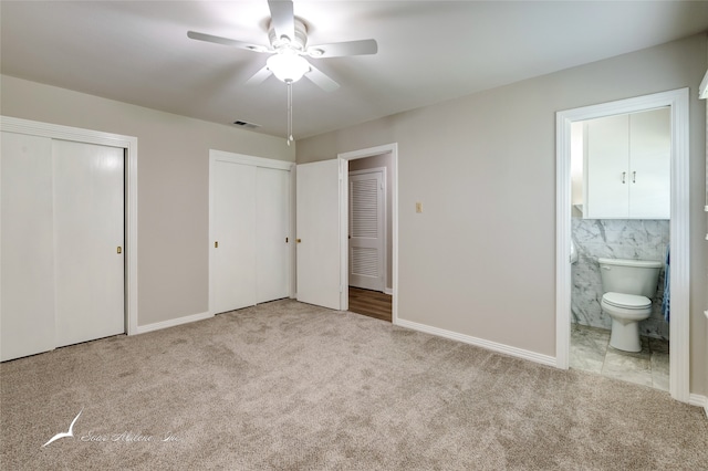 unfurnished bedroom featuring connected bathroom, ceiling fan, light colored carpet, and multiple closets