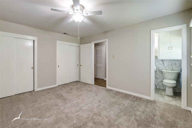 unfurnished bedroom with light carpet, ensuite bathroom, ceiling fan, tile walls, and multiple closets