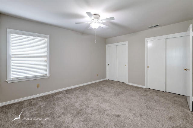 unfurnished bedroom with light colored carpet, ceiling fan, and multiple closets