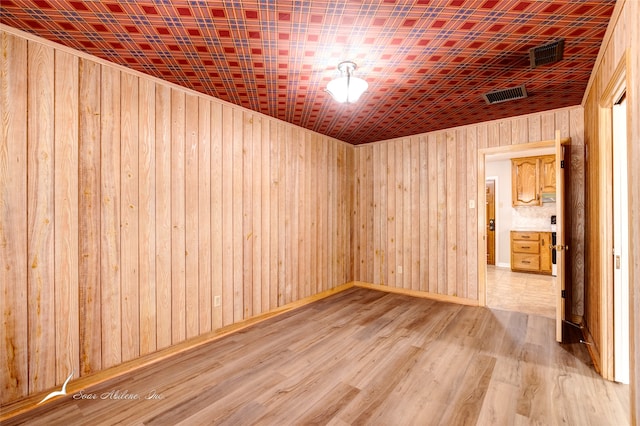 empty room with light wood-type flooring and wooden walls