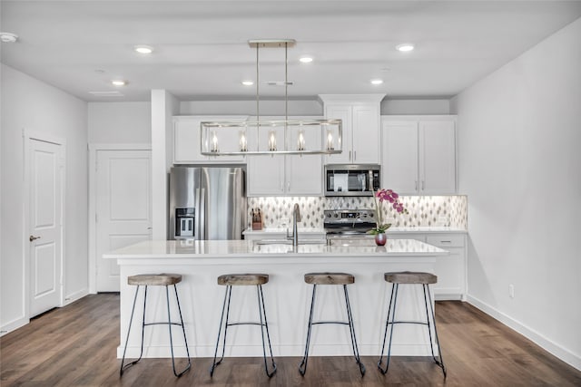 kitchen with dark wood-type flooring, white cabinets, hanging light fixtures, an island with sink, and appliances with stainless steel finishes