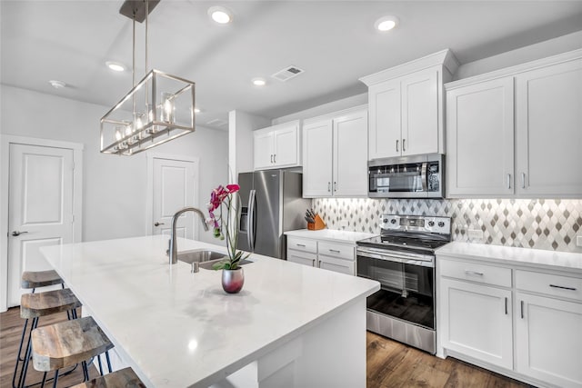 kitchen with decorative light fixtures, stainless steel appliances, a kitchen island with sink, and sink