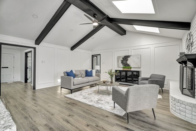 living room with a fireplace, lofted ceiling with skylight, light hardwood / wood-style flooring, and ceiling fan