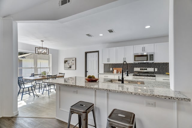 kitchen with kitchen peninsula, appliances with stainless steel finishes, sink, white cabinets, and hanging light fixtures