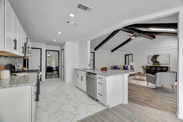 kitchen featuring white cabinetry, sink, stainless steel appliances, light stone counters, and lofted ceiling with beams