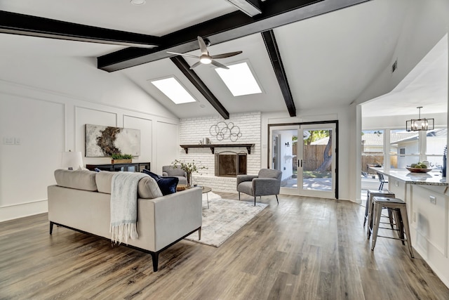 living room with a fireplace, vaulted ceiling with skylight, wood-type flooring, and ceiling fan with notable chandelier