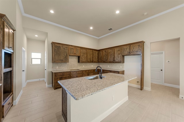 kitchen with an island with sink, light stone countertops, sink, and backsplash