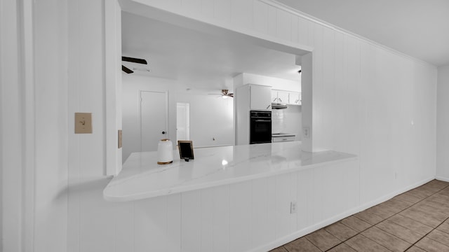 kitchen with kitchen peninsula, light stone counters, black double oven, white cabinets, and light tile patterned flooring