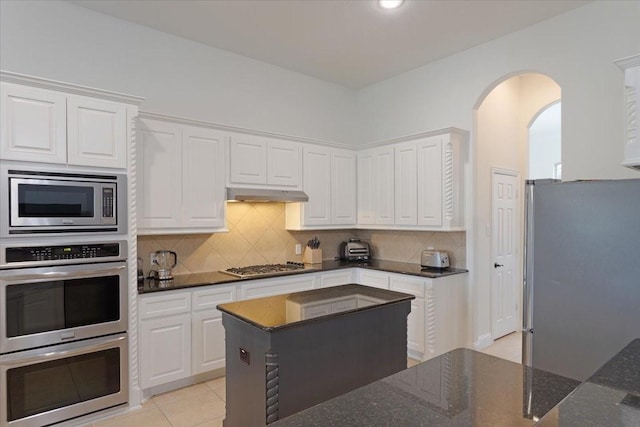 kitchen featuring light tile patterned floors, dark stone countertops, decorative backsplash, white cabinets, and appliances with stainless steel finishes