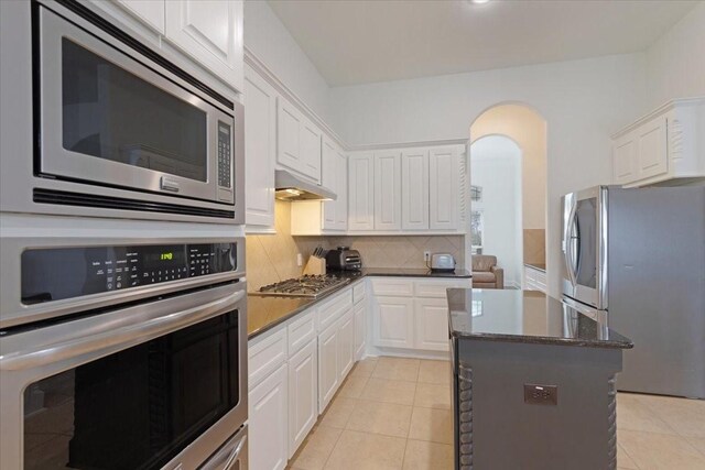 kitchen with a center island, decorative backsplash, appliances with stainless steel finishes, light tile patterned flooring, and white cabinetry