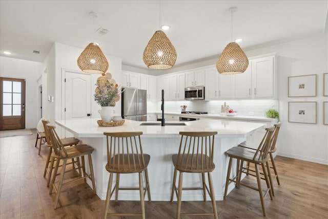 kitchen featuring appliances with stainless steel finishes, white cabinetry, a kitchen island with sink, and sink