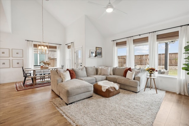 living room featuring ceiling fan with notable chandelier, high vaulted ceiling, and light hardwood / wood-style flooring