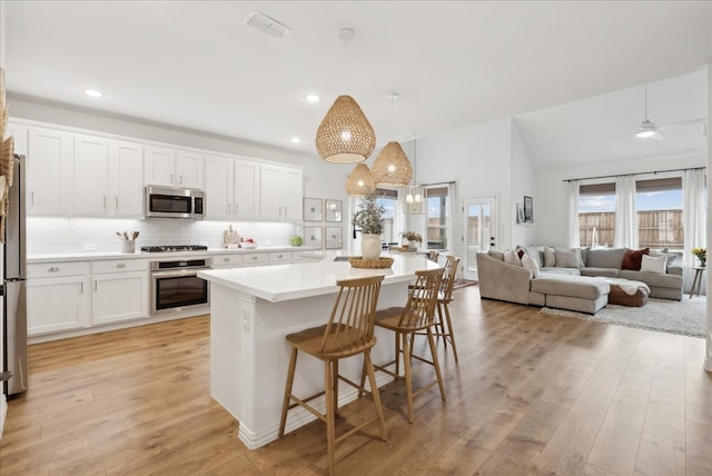 kitchen with appliances with stainless steel finishes, decorative light fixtures, light hardwood / wood-style flooring, white cabinets, and a kitchen island