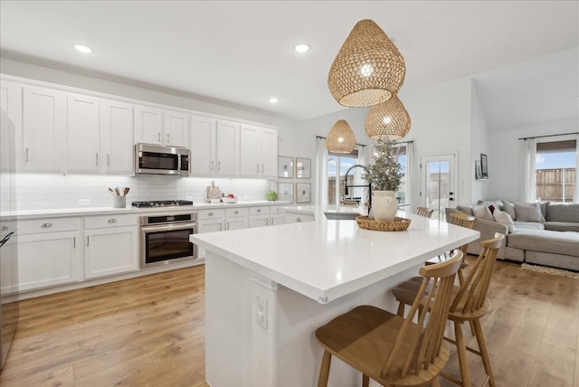 kitchen with a kitchen breakfast bar, sink, hanging light fixtures, light hardwood / wood-style flooring, and stainless steel appliances