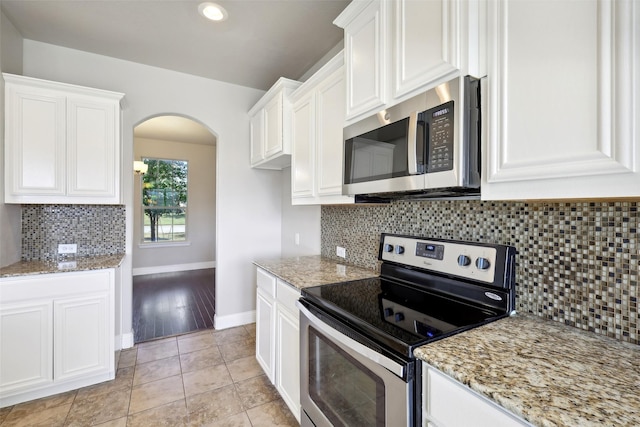 kitchen featuring light tile patterned floors, light stone countertops, appliances with stainless steel finishes, tasteful backsplash, and white cabinetry