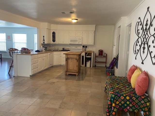 kitchen featuring a kitchen bar, white appliances, sink, white cabinets, and a center island