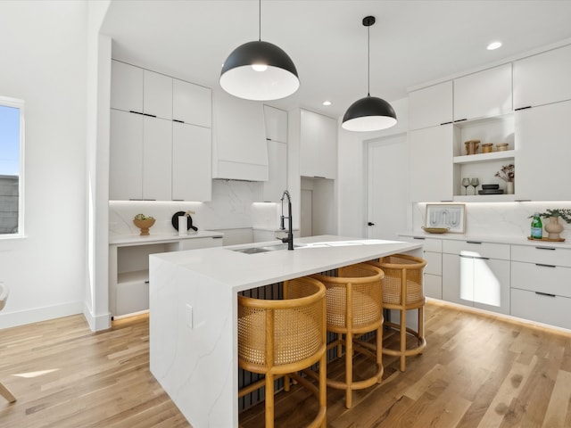 kitchen featuring a center island with sink, light hardwood / wood-style floors, white cabinetry, and hanging light fixtures