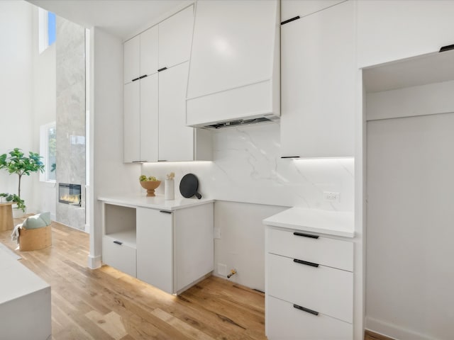 kitchen featuring a tile fireplace, backsplash, light hardwood / wood-style floors, and white cabinetry