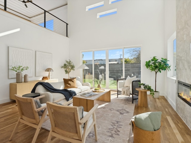 living room with light hardwood / wood-style floors, a towering ceiling, and a tiled fireplace