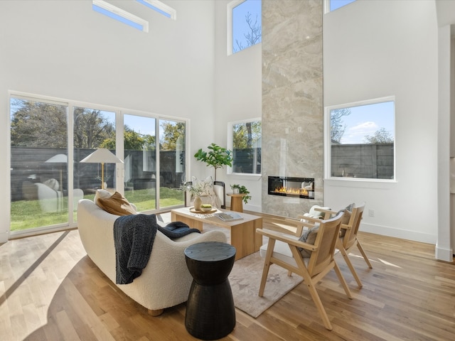 living room featuring light wood-type flooring, a towering ceiling, and a tiled fireplace