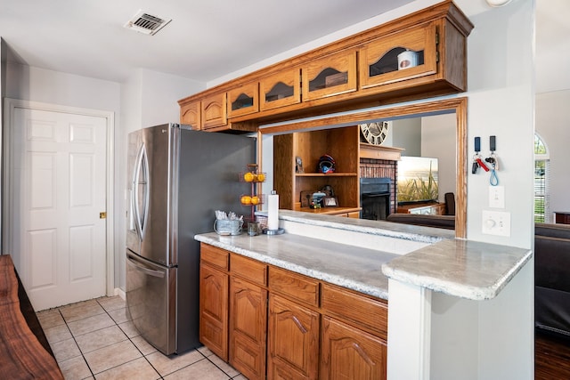 kitchen with light tile patterned flooring, visible vents, stainless steel fridge with ice dispenser, brown cabinetry, and glass insert cabinets