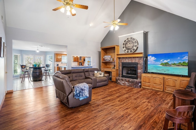 living area featuring light wood finished floors, a fireplace, high vaulted ceiling, and a ceiling fan