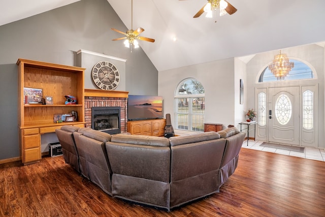 living area with high vaulted ceiling, ceiling fan with notable chandelier, dark wood-style flooring, a fireplace, and baseboards