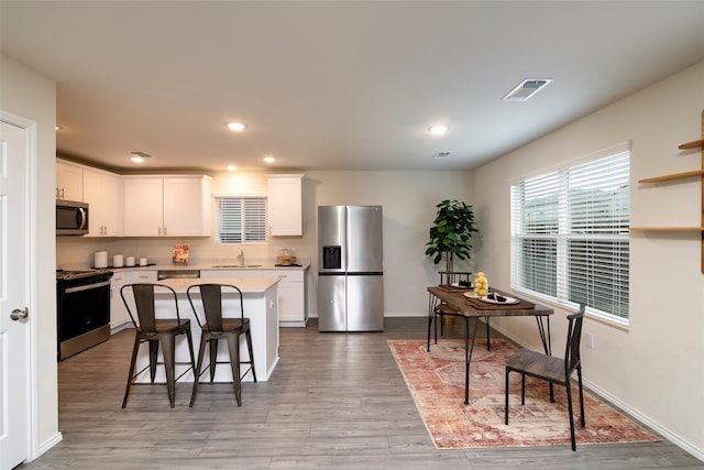 kitchen with a kitchen breakfast bar, a kitchen island, white cabinets, and appliances with stainless steel finishes